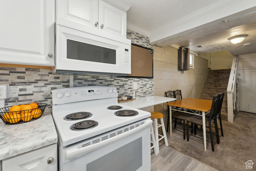 Kitchen featuring white appliances, ornamental molding, white cabinetry, decorative backsplash, and light wood-style floors