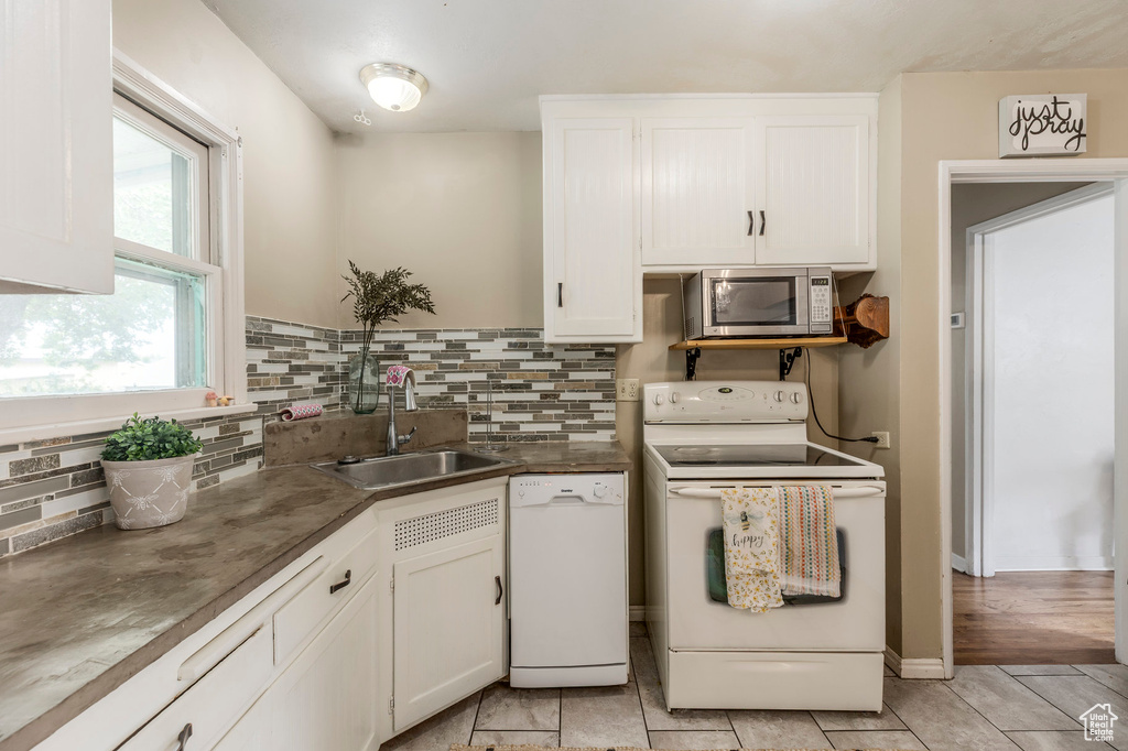 Kitchen with white appliances, a sink, white cabinetry, backsplash, and dark countertops
