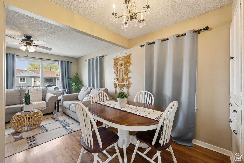 Dining space with a textured ceiling, wood finished floors, ceiling fan with notable chandelier, and baseboards