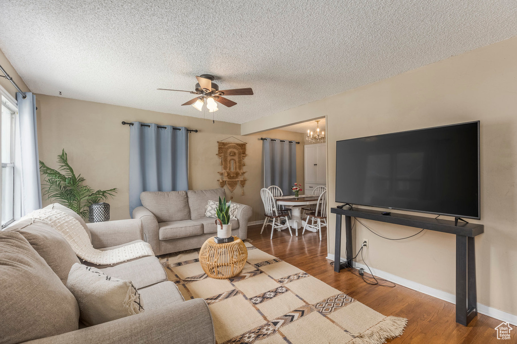 Living area featuring ceiling fan, wood finished floors, a textured ceiling, a chandelier, and baseboards