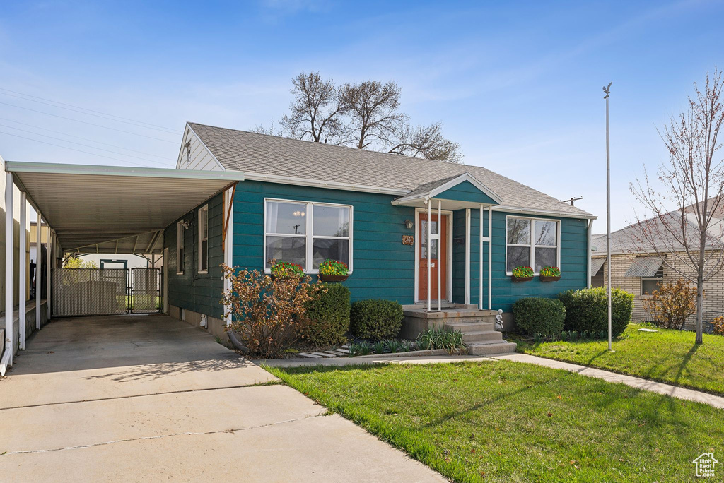 View of front of house with a shingled roof, an attached carport, a front lawn, a gate, and driveway