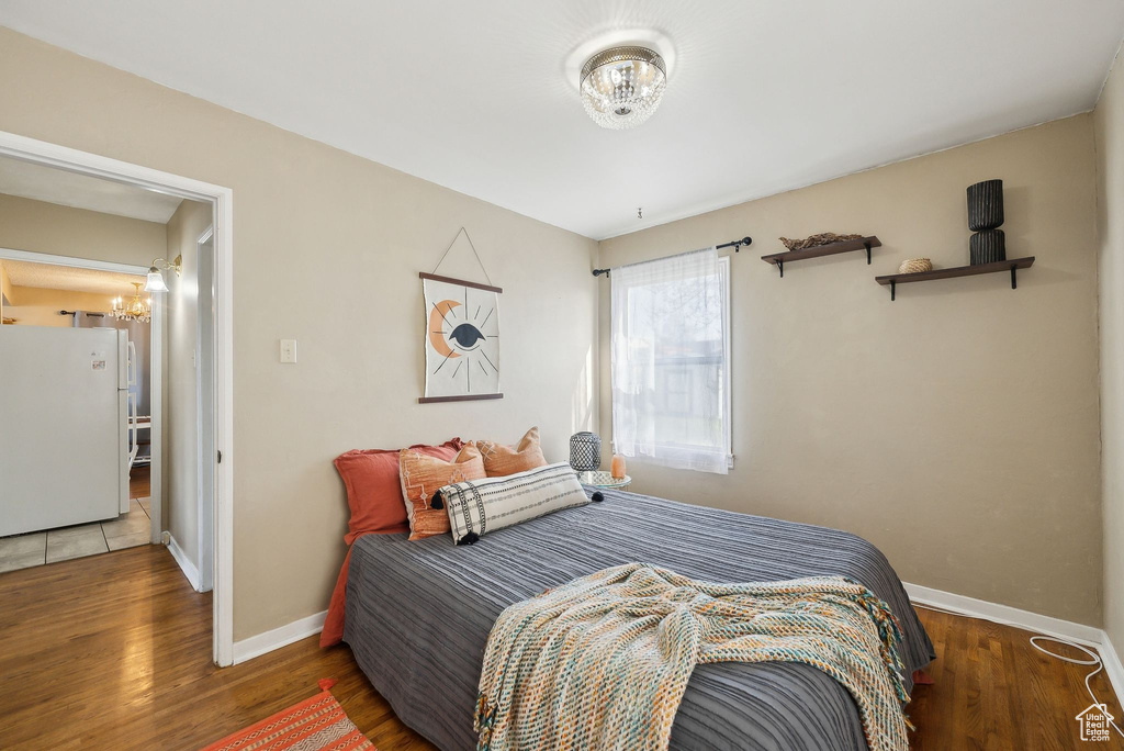 Bedroom featuring wood finished floors, freestanding refrigerator, a notable chandelier, and baseboards
