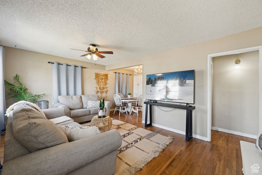Living area featuring ceiling fan with notable chandelier, a textured ceiling, baseboards, and dark wood-style floors