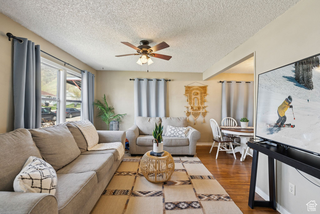 Living room featuring ceiling fan, baseboards, wood finished floors, and a textured ceiling