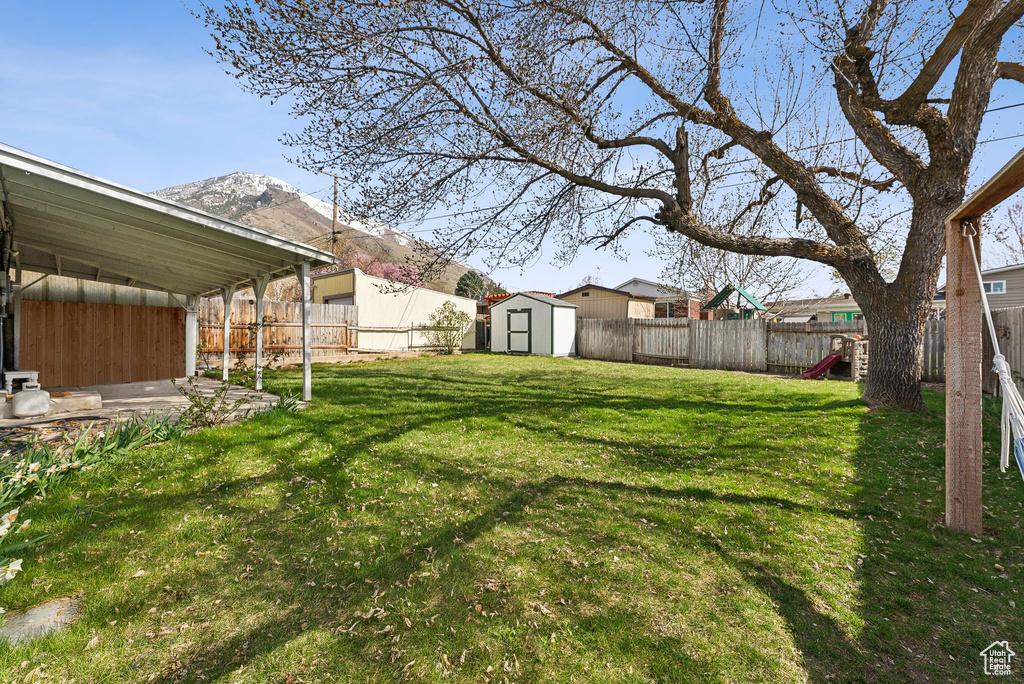 View of yard with a storage shed, a fenced backyard, a mountain view, and an outbuilding