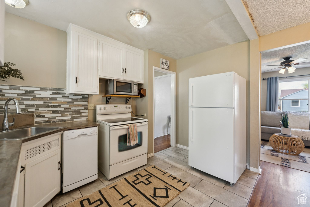 Kitchen featuring white appliances, white cabinets, ceiling fan, decorative backsplash, and a sink