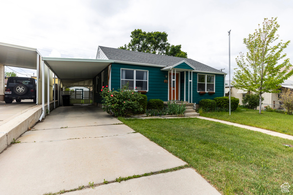 View of front of property featuring a front yard, an attached carport, driveway, and a shingled roof