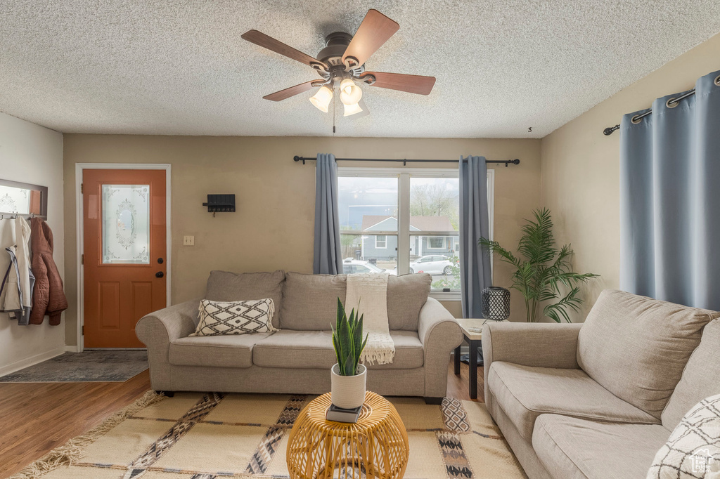 Living room with light wood-style flooring, a ceiling fan, a textured ceiling, and baseboards