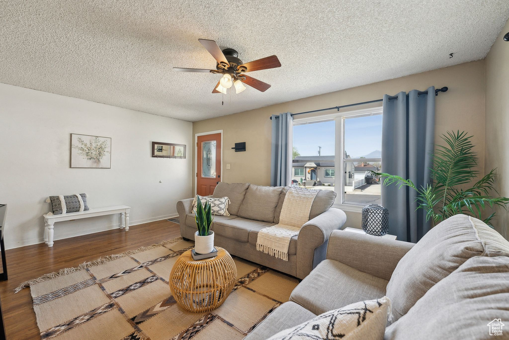 Living area featuring baseboards, a ceiling fan, wood finished floors, and a textured ceiling