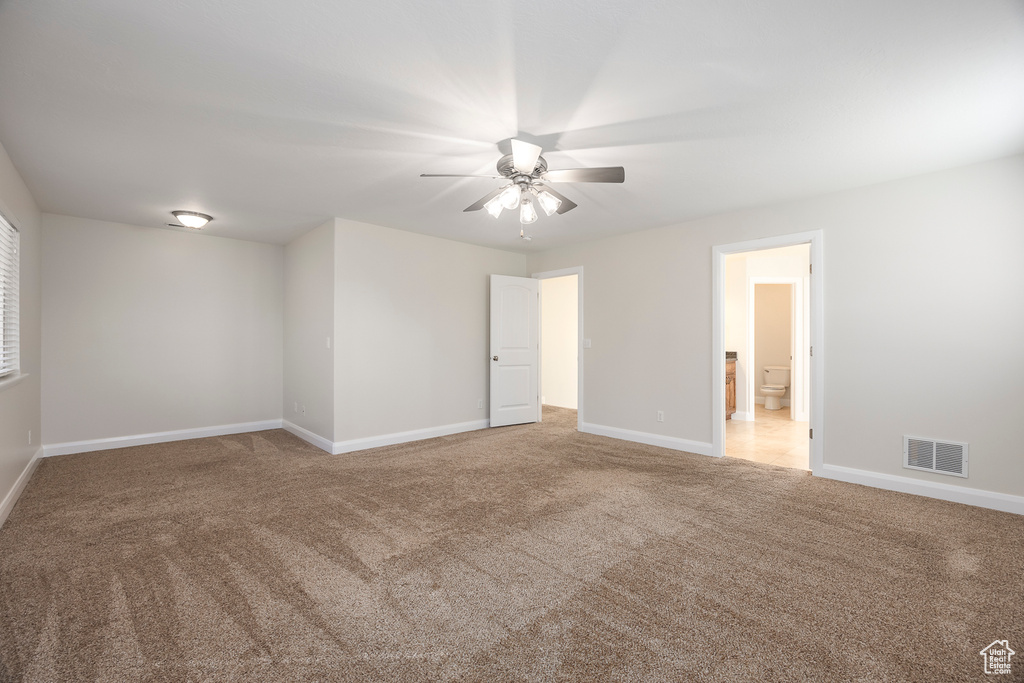 Empty room with carpet, visible vents, baseboards, and a ceiling fan