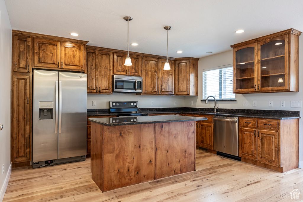 Kitchen with glass insert cabinets, a center island, light wood-style floors, stainless steel appliances, and pendant lighting