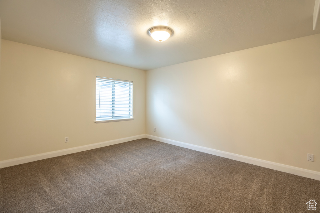 Empty room featuring baseboards, dark carpet, and a textured ceiling