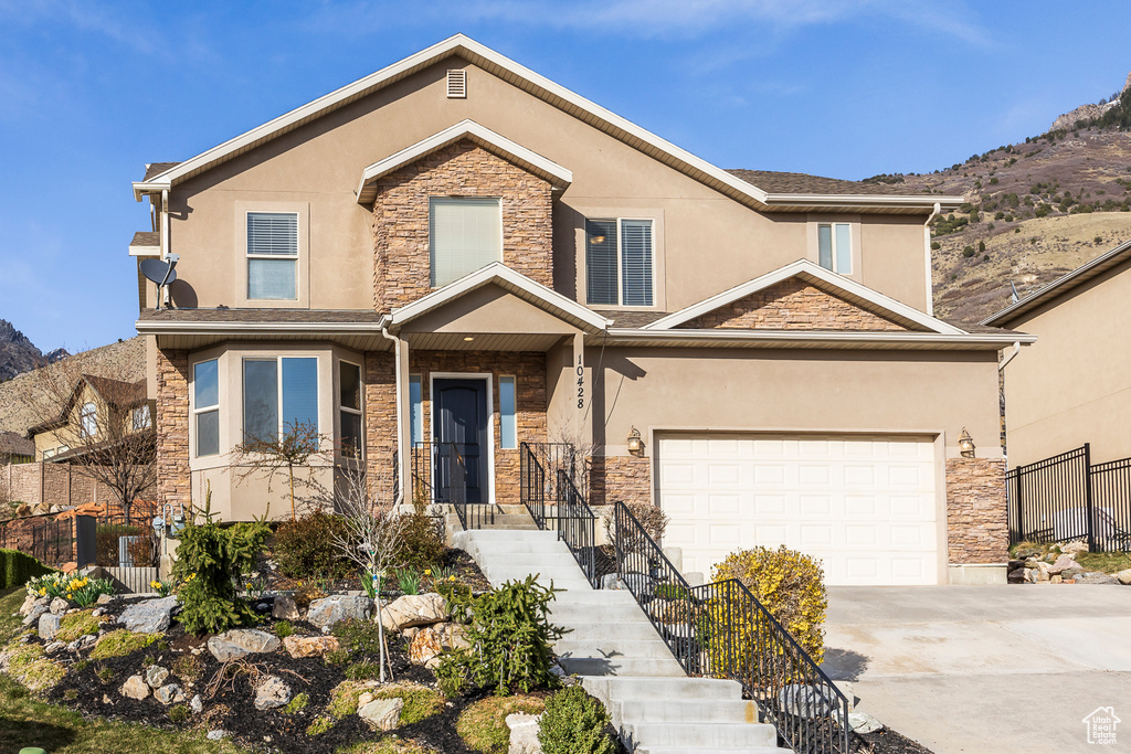 View of front of house featuring a garage, stucco siding, fence, stone siding, and driveway