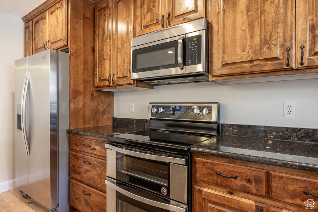 Kitchen featuring stainless steel appliances, brown cabinets, and dark stone counters