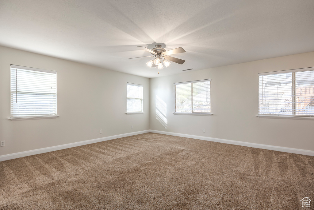 Carpeted spare room with visible vents, ceiling fan, and baseboards