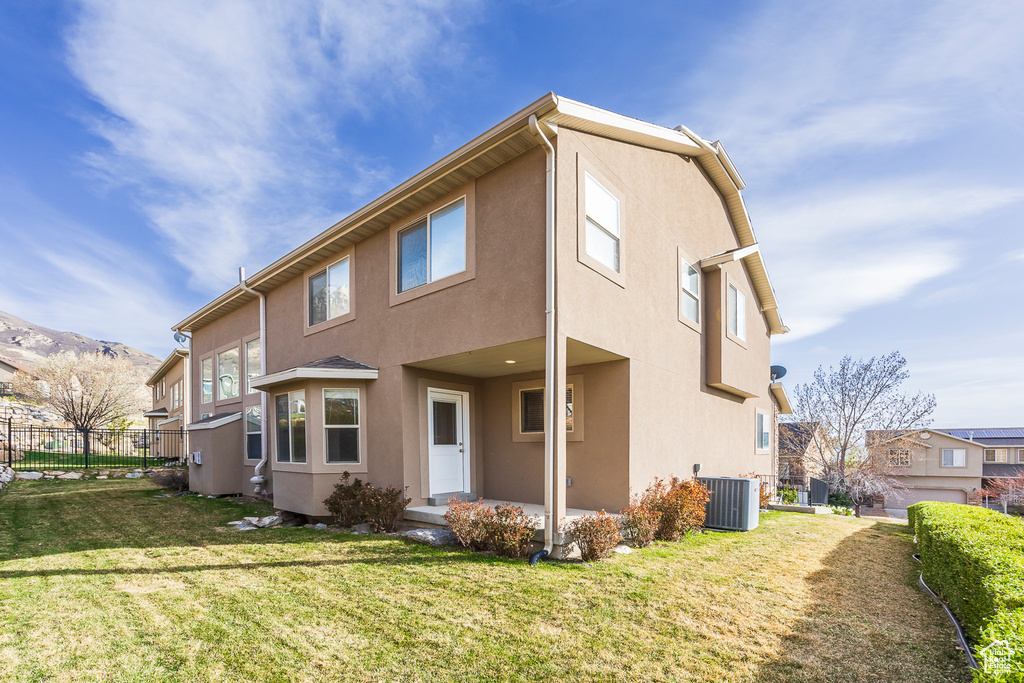 Back of property featuring central air condition unit, stucco siding, fence, and a lawn