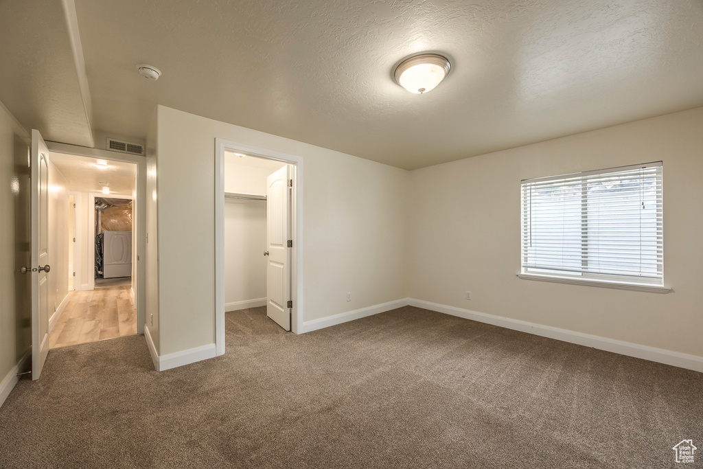 Unfurnished bedroom featuring baseboards, a walk in closet, washer / dryer, visible vents, and carpet