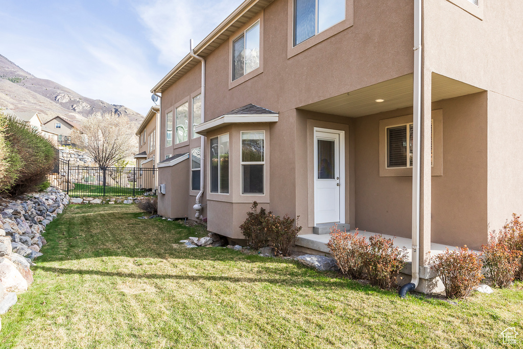 Back of property with a yard, stucco siding, fence, and a mountain view