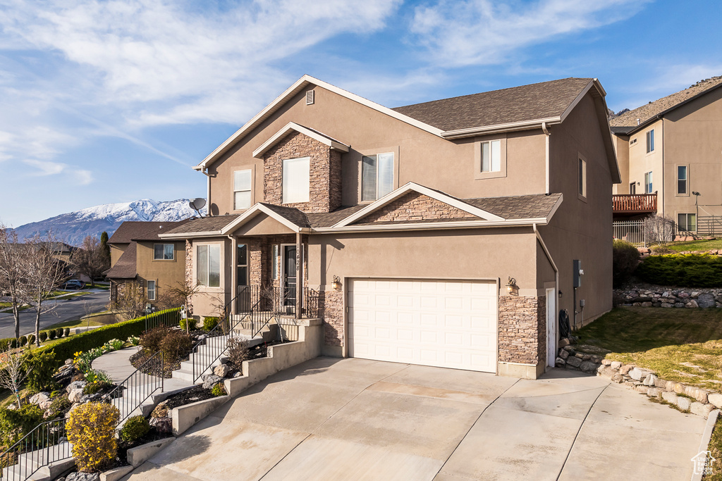 View of front facade featuring a mountain view, stucco siding, stone siding, and concrete driveway