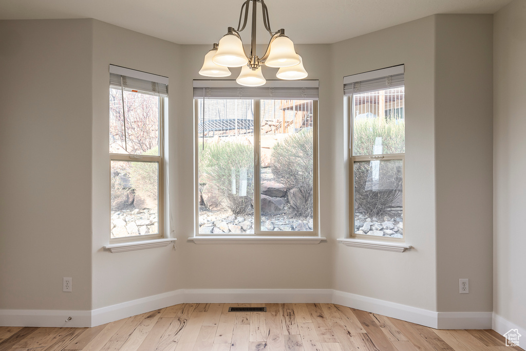 Unfurnished dining area with wood finished floors, an inviting chandelier, baseboards, and visible vents