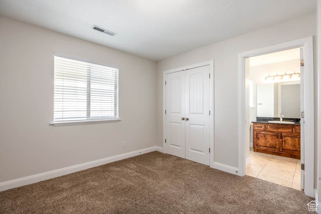 Unfurnished bedroom with a closet, light colored carpet, visible vents, a sink, and baseboards