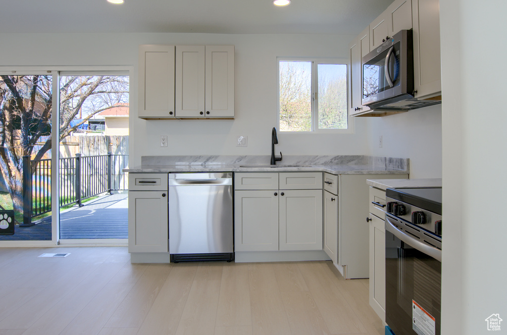 Kitchen featuring a sink, appliances with stainless steel finishes, recessed lighting, light wood finished floors, and light stone counters