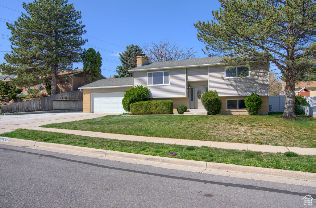 Raised ranch featuring a front yard, fence, an attached garage, a chimney, and driveway