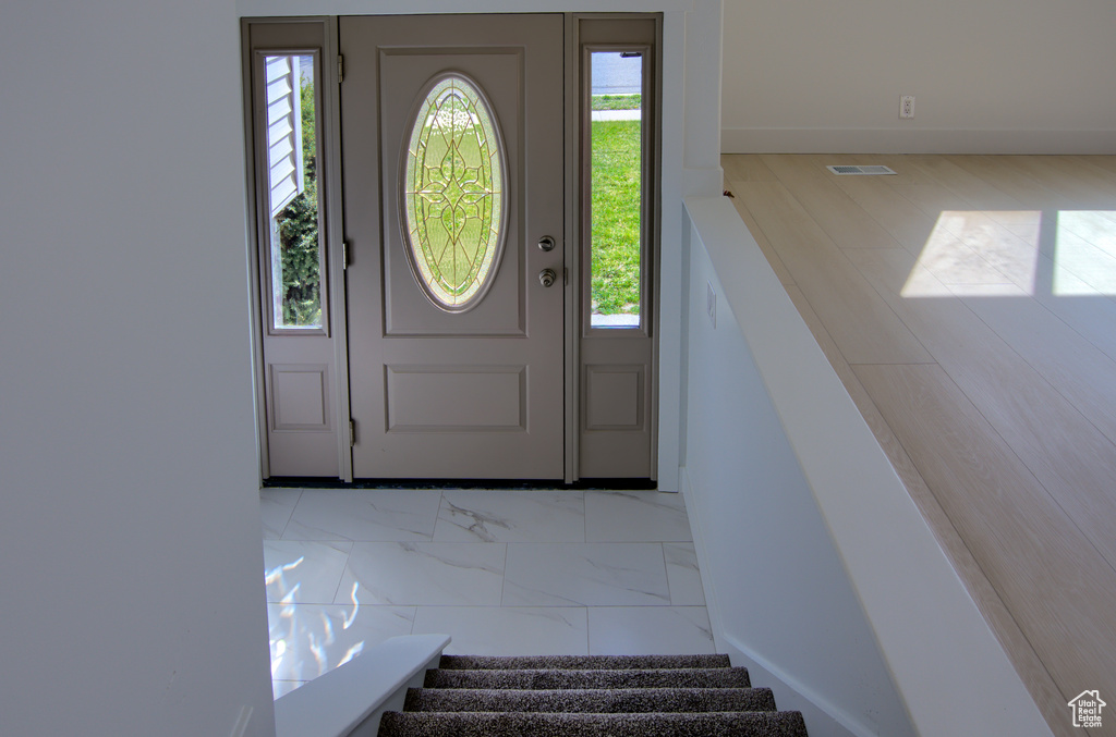 Foyer entrance with marble finish floor, stairs, visible vents, and plenty of natural light