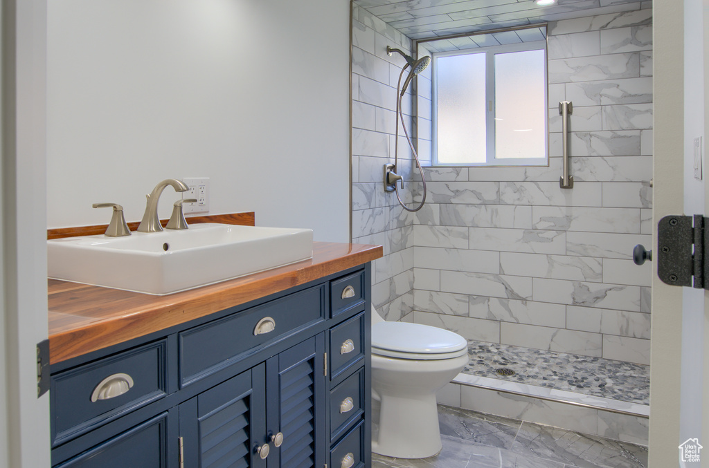 Bathroom featuring vanity, marble finish floor, a tile shower, and toilet