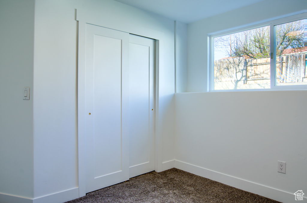 Unfurnished bedroom featuring dark carpet, a closet, and baseboards
