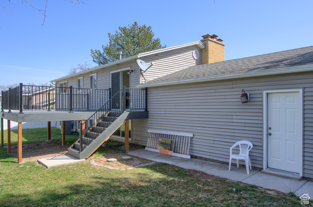 Rear view of property featuring a yard, a deck, a chimney, and stairs