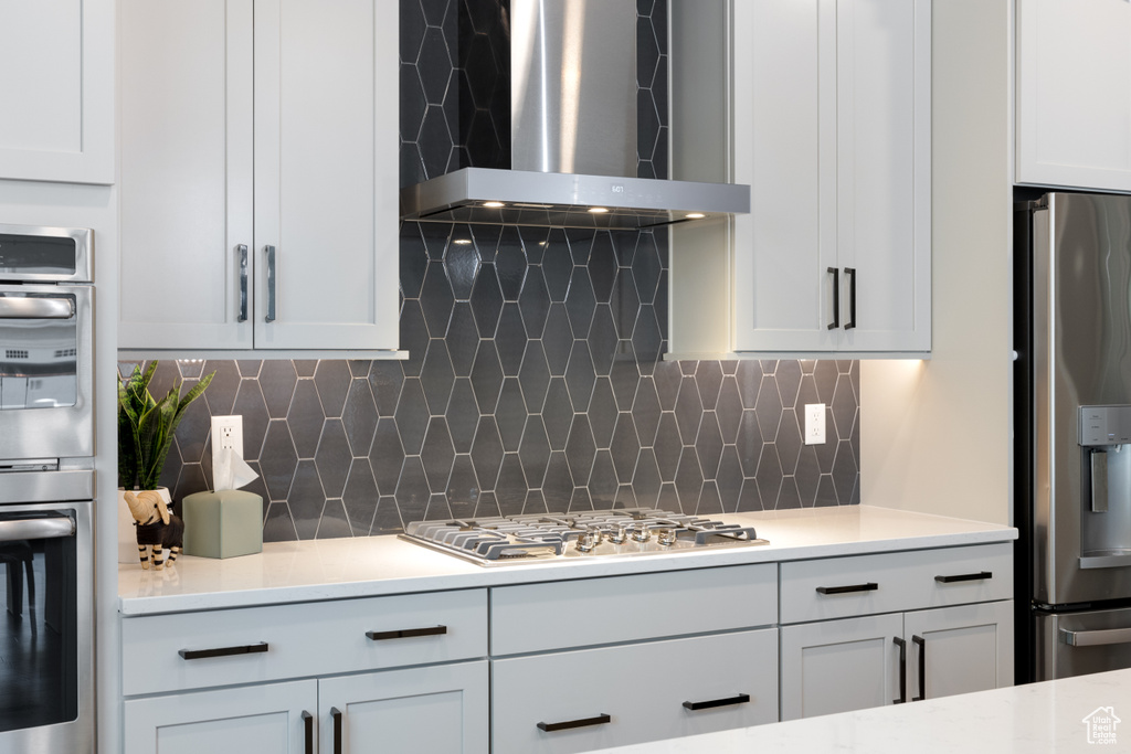 Kitchen featuring appliances with stainless steel finishes, wall chimney range hood, light countertops, and tasteful backsplash