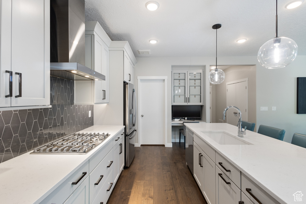 Kitchen featuring wall chimney exhaust hood, appliances with stainless steel finishes, a sink, backsplash, and dark wood-type flooring