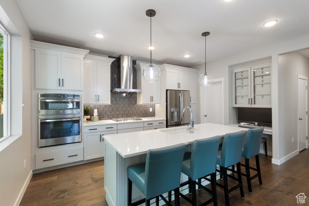 Kitchen with wall chimney exhaust hood, appliances with stainless steel finishes, backsplash, a breakfast bar, and recessed lighting