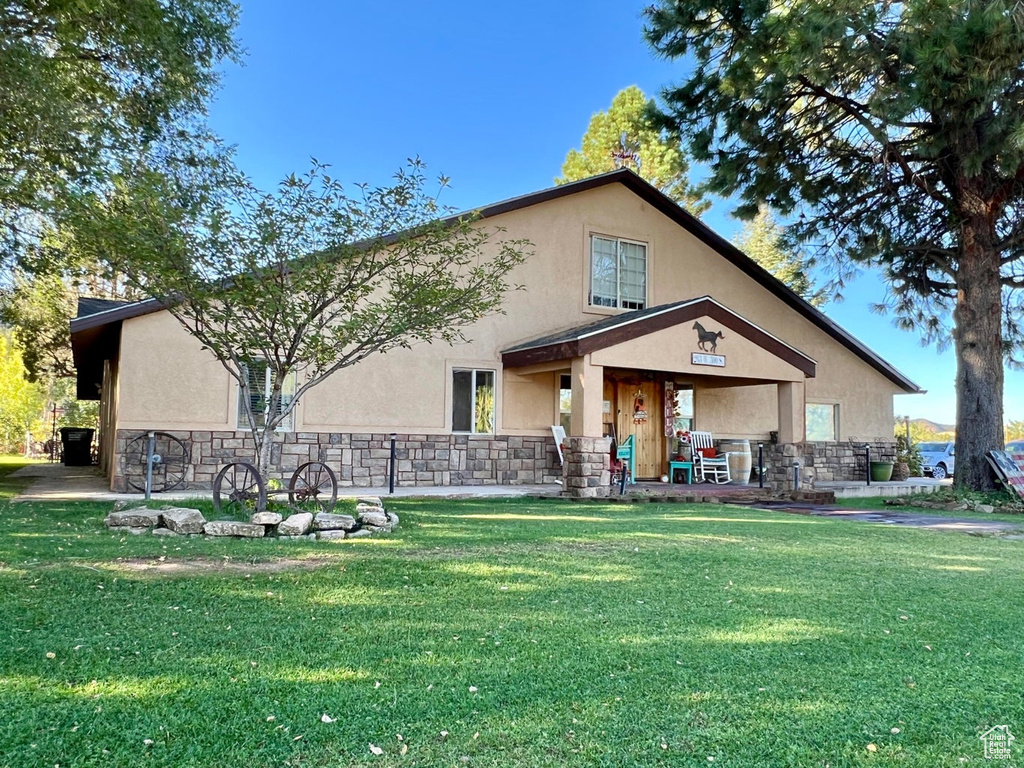 Rear view of house with stucco siding, a yard, stone siding, and a porch