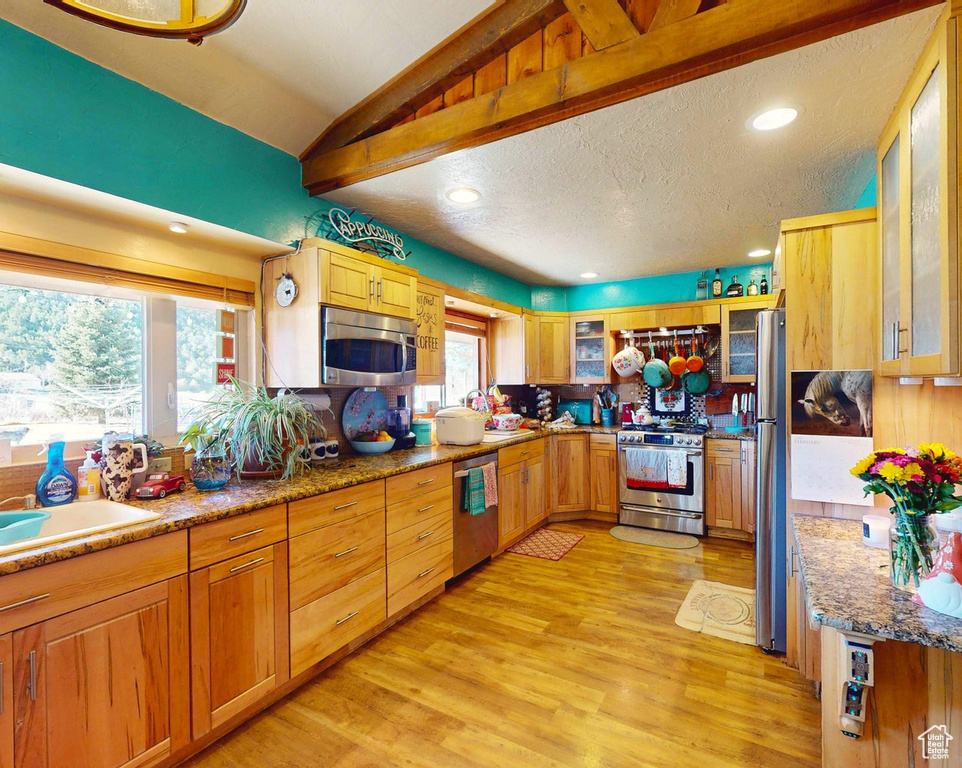 Kitchen with appliances with stainless steel finishes, light wood-style floors, glass insert cabinets, vaulted ceiling, and recessed lighting