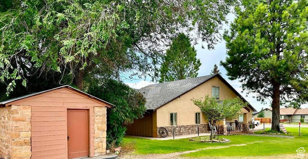 Exterior space with stone siding, a storage unit, a yard, and a shingled roof