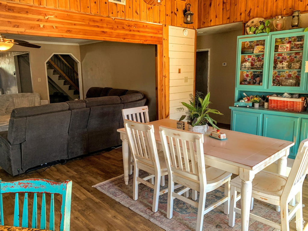 Dining room featuring dark wood finished floors, ceiling fan, stairway, and wood walls