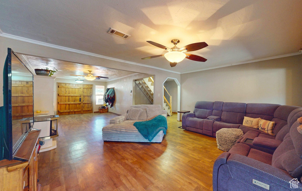 Living area with ceiling fan, wood finished floors, stairway, and crown molding