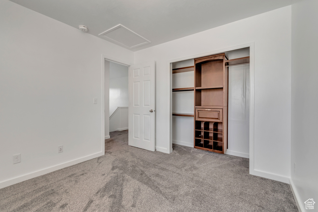 Unfurnished bedroom with carpet floors, attic access, baseboards, and a closet