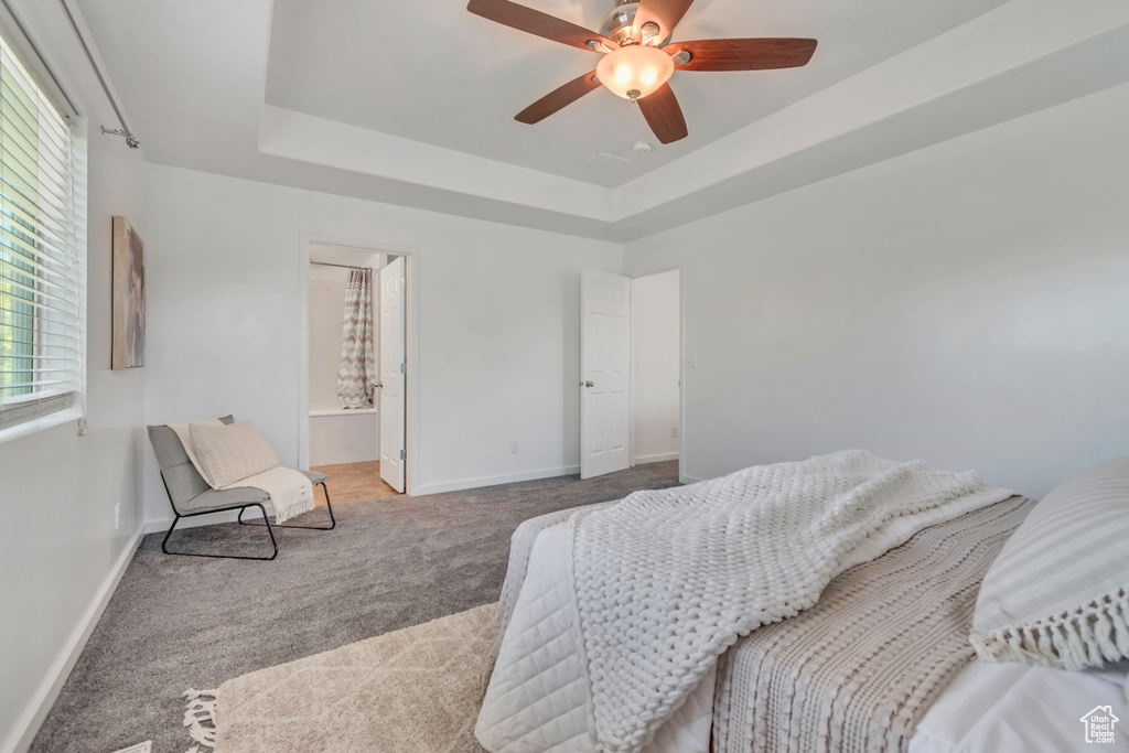 Carpeted bedroom with baseboards, a tray ceiling, a ceiling fan, and ensuite bath