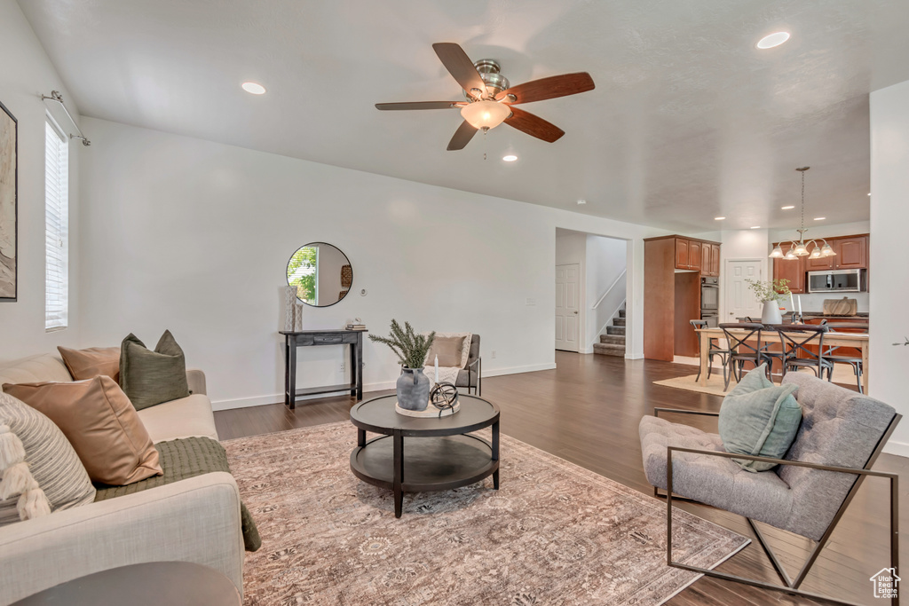 Living room featuring stairs, dark wood-type flooring, a ceiling fan, a chandelier, and recessed lighting