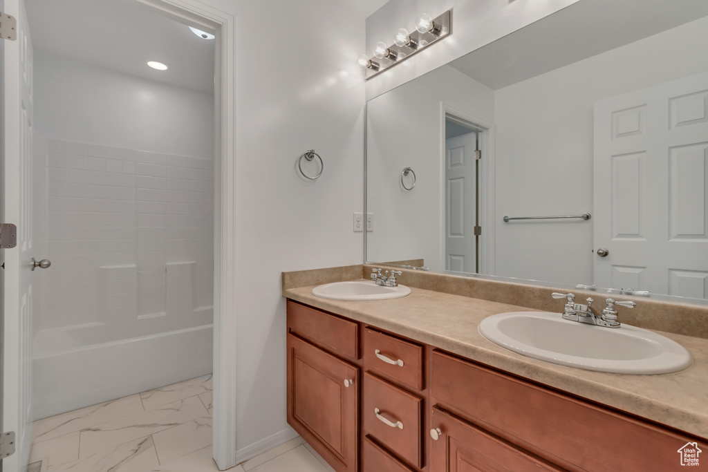 Full bath featuring double vanity, marble look tile flooring, shower / bathtub combination, and baseboards