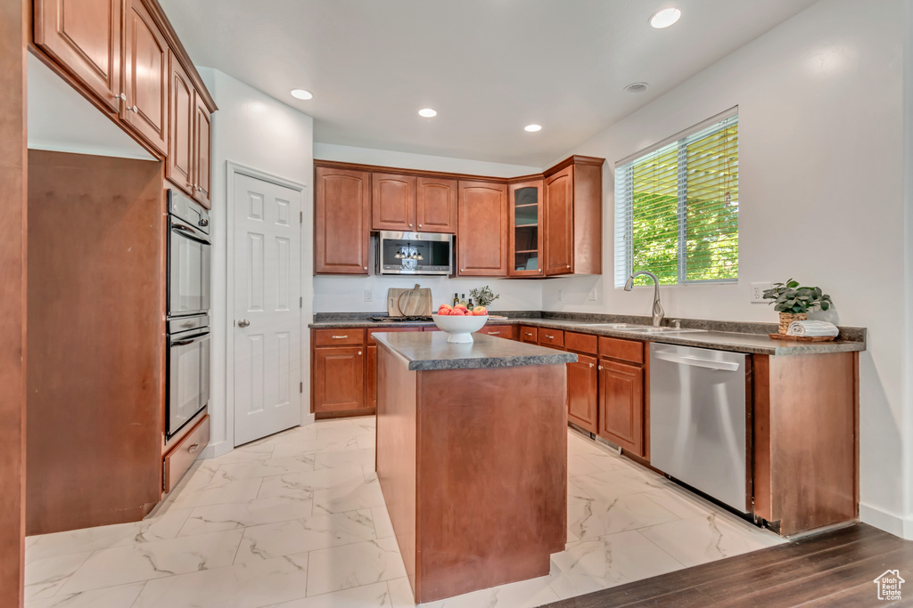 Kitchen featuring appliances with stainless steel finishes, a sink, dark countertops, light marble finish flooring, and recessed lighting