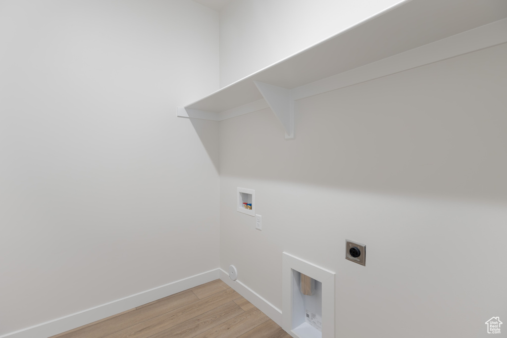 Clothes washing area with hookup for a washing machine, hookup for an electric dryer, light wood-style floors, and baseboards