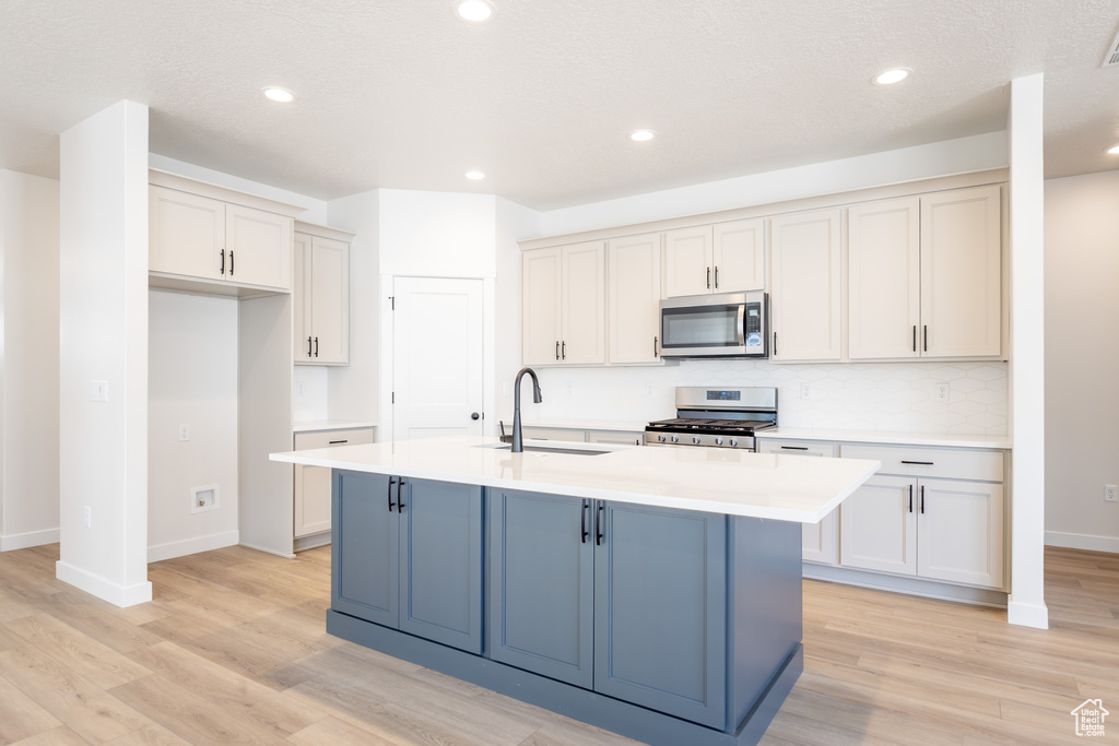 Kitchen featuring appliances with stainless steel finishes, a sink, light countertops, light wood-style floors, and baseboards
