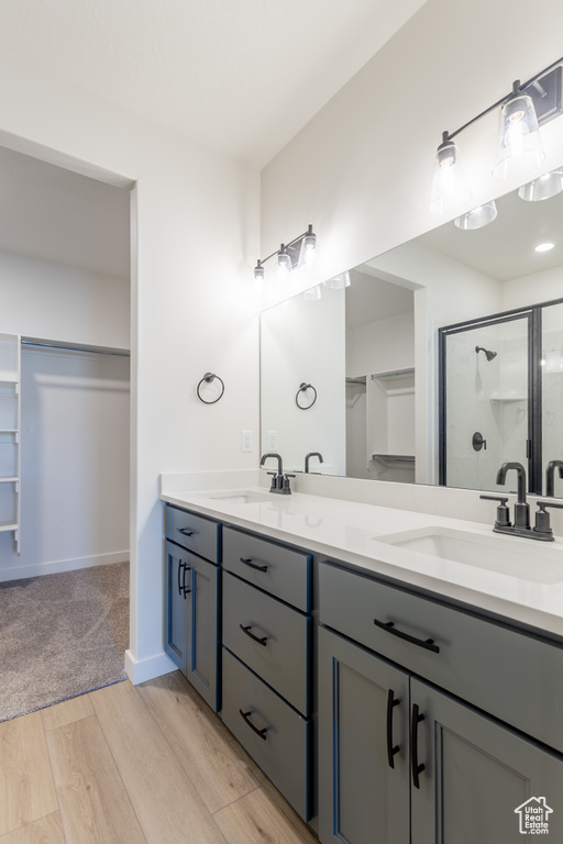 Bathroom featuring a stall shower, wood finished floors, double vanity, and a walk in closet