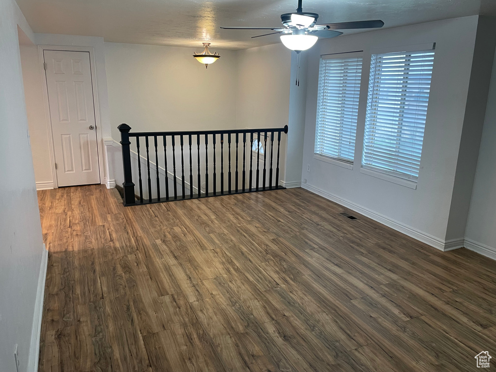 Unfurnished room with dark wood-type flooring, visible vents, ceiling fan, and baseboards