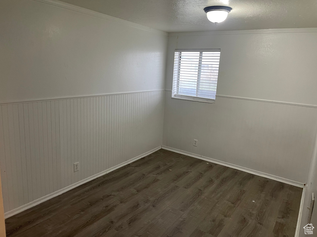 Unfurnished room with a textured ceiling, crown molding, dark wood finished floors, and a wainscoted wall