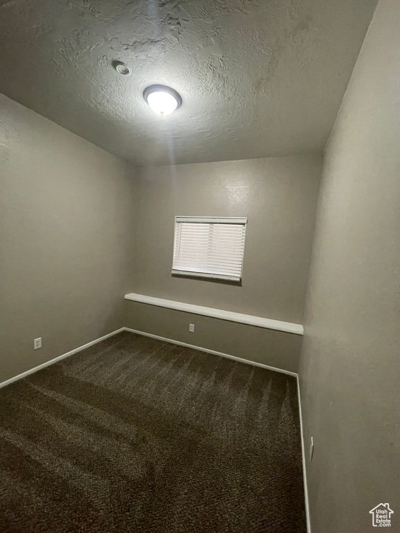 Empty room featuring dark carpet, a textured ceiling, and baseboards